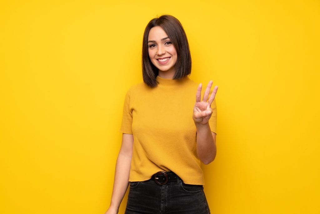 Young woman over yellow wall happy and counting three with fingers